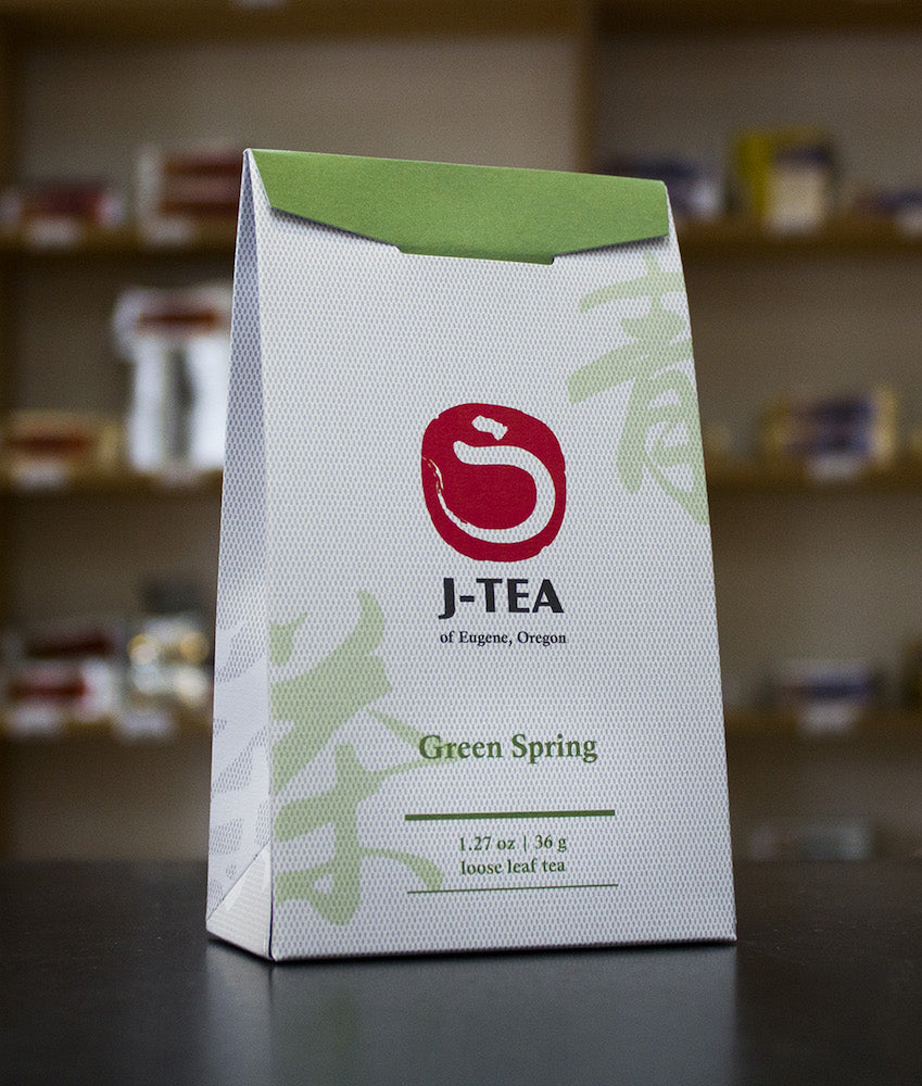J-Tea Green Spring Taiwan Oolong tea package on a dark surface with a blurred background